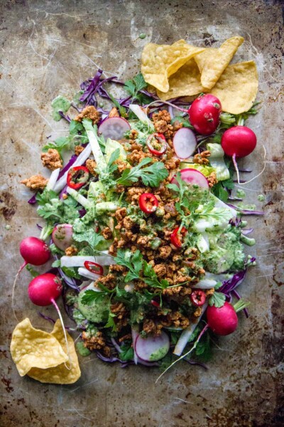 A pile of turkey taco salad piled up on a stainless steel sheet, with radishes, lettuce, cabbage, cilantro, and tortilla chips.