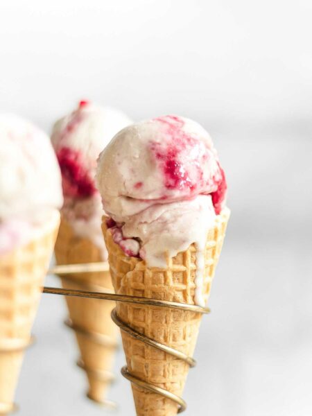 A close-up of 3 raspberry ripple ice cream in waffle cones.
