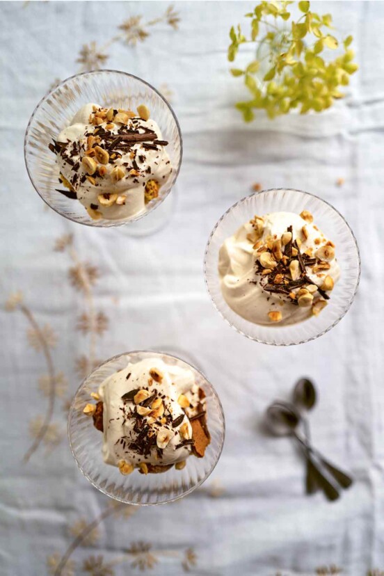 Three glass bowls filled with coffee mousse sprinkled with nuts, on a white tablecloth.