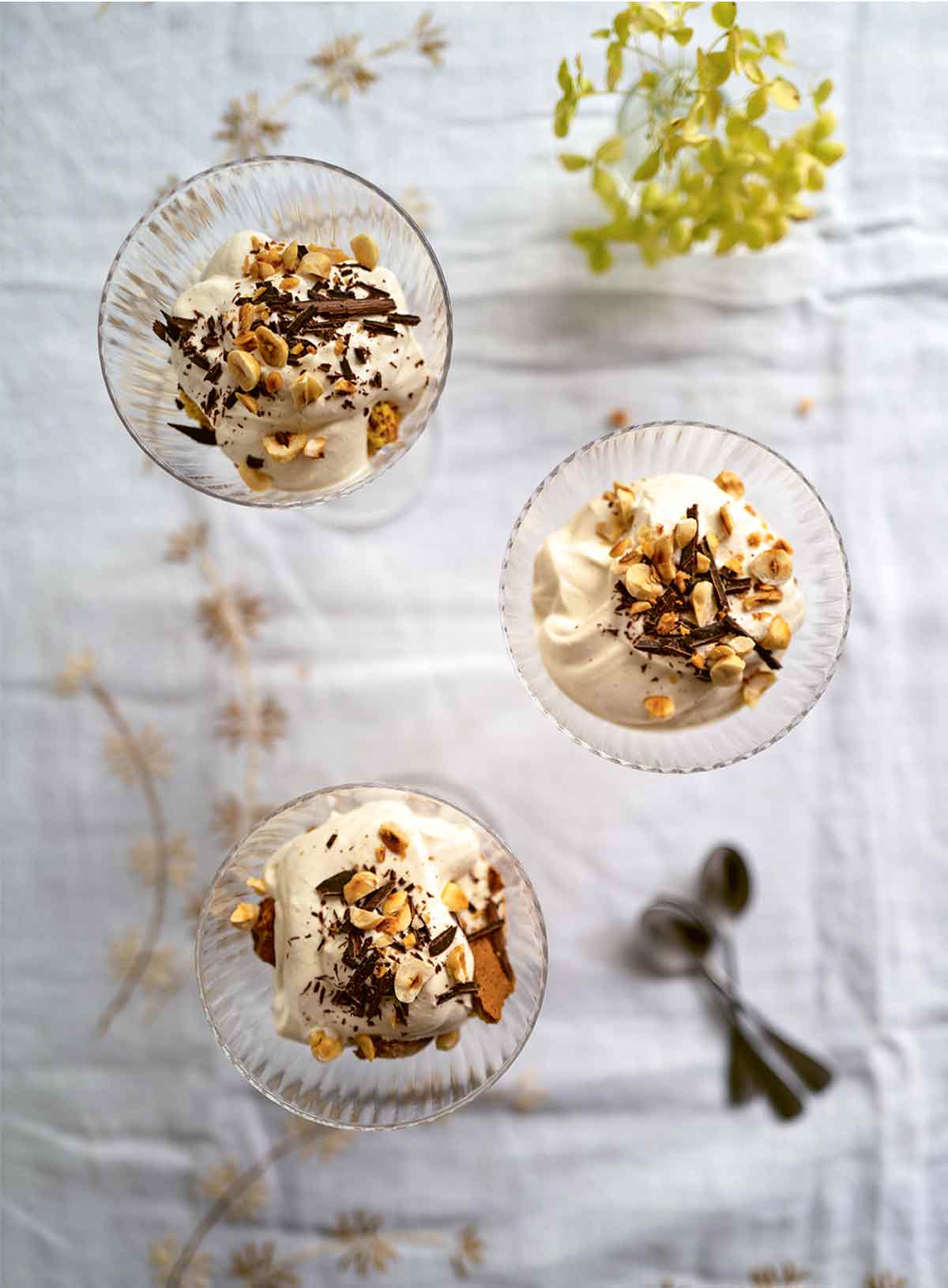 Three glass bowls filled with coffee mousse sprinkled with nuts, on a white tablecloth.