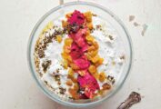 A bowl of yogurt and cucumber dip, topped with golden raisins, mint, and rose petals.