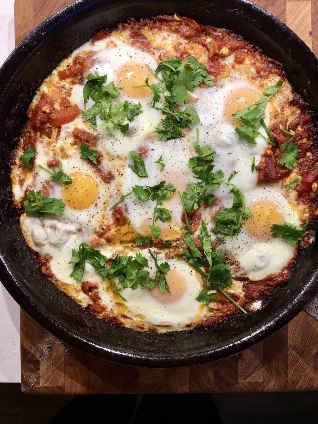 A cast-iron skillet with 6 eggs in tomato sauce and sprinkled with parsley.