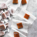 5 unwrapped squares of apple cider caramels beside a pile of wrapped caramels.