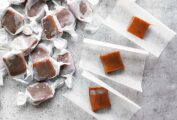 5 unwrapped squares of apple cider caramels beside a pile of wrapped caramels.