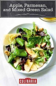 A large white bowl filled with apples, parmesan, walnuts, and mixed green salad.