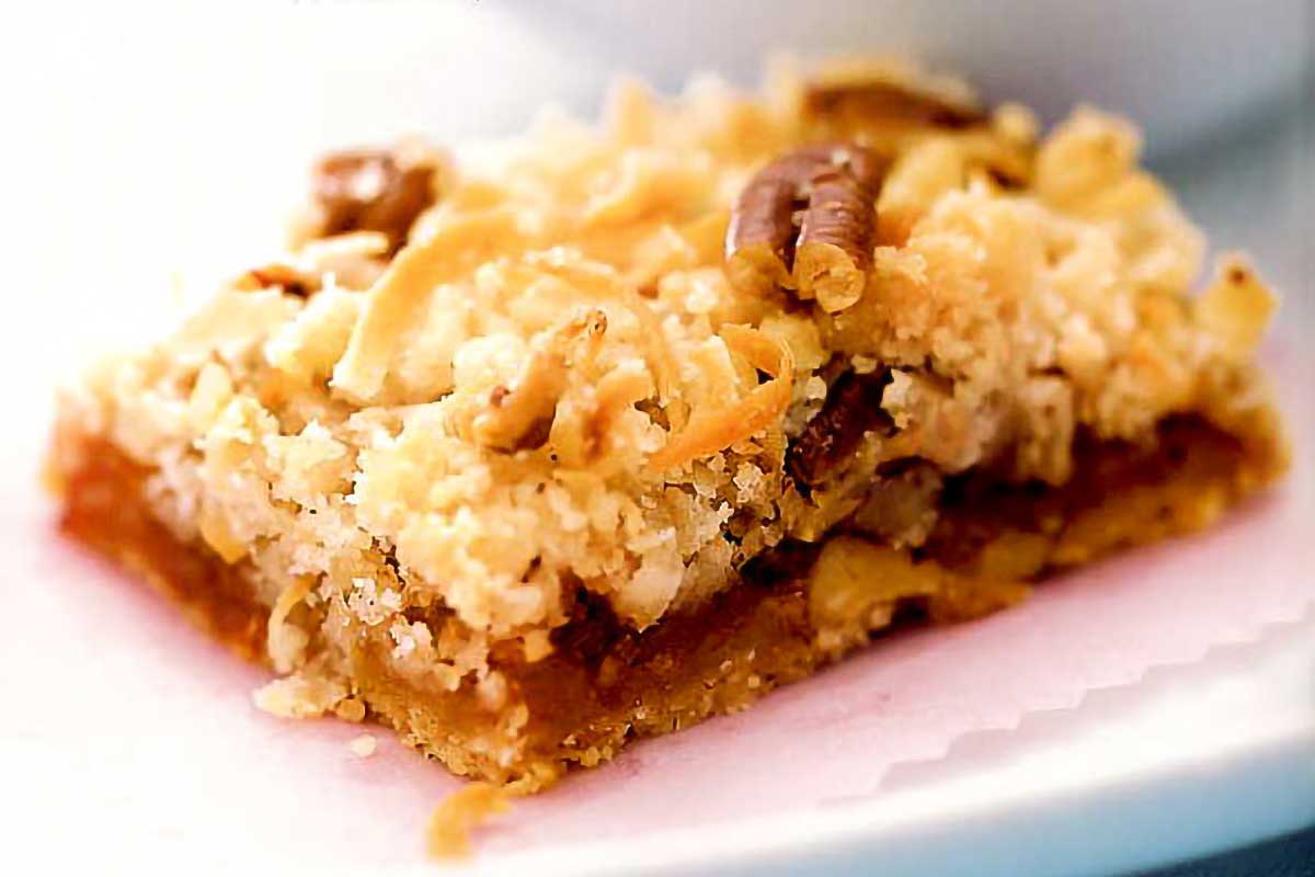 A white plate with a square of apricot cherry coconut bar topped with pecans.