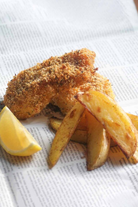 2 pieces of panko coated fish with chips and a slice of lemon, laying of a sheet of newspaper