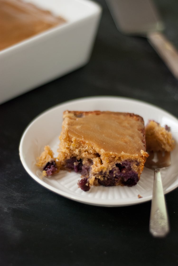 A white dessert plate and spoon with a square of blueberry maple tea cake.