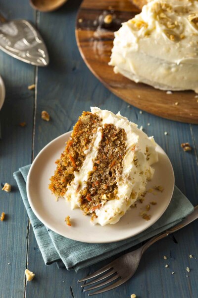 A slice of classic carrot cake--two carrot cake layers filled and frosted with cream cheese frosting; on top are crushed walnuts.