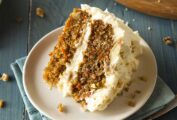 A slice of classic carrot cake--two carrot cake layers filled and frosted with cream cheese frosting; on top are crushed walnuts.