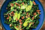 A blue bowl filled with kale, pecans, green apple, and cilantro on a wooden table.