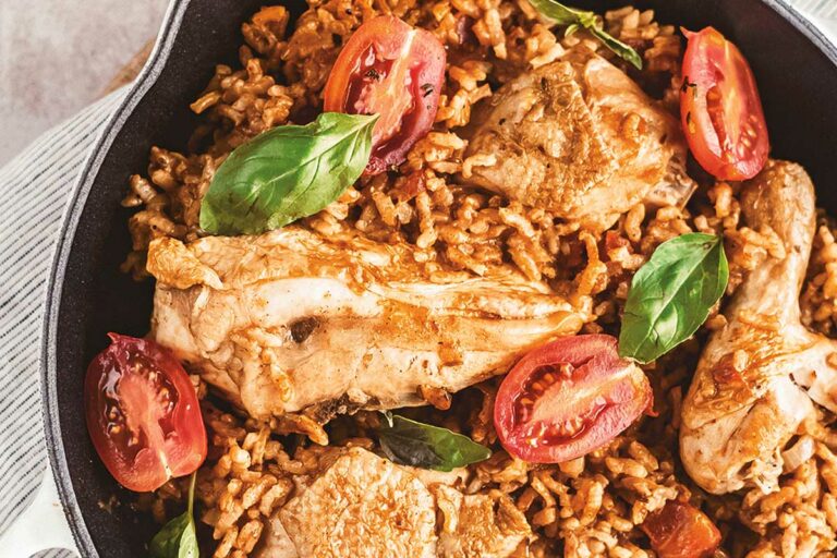 A cast-iron skillet with chicken, orzo, tomatoes, and garnished with basil.