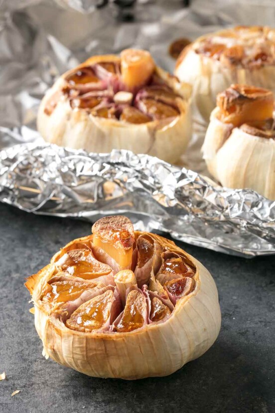 4 bulbs of roasted garlic with the tops cut off, 3 lying on a sheet of aluminium foil.