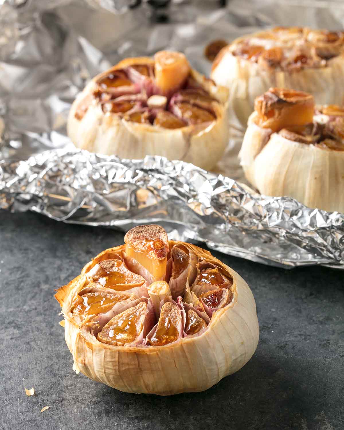 4 bulbs of roasted garlic with the tops cut off, 3 lying on a sheet of aluminium foil.