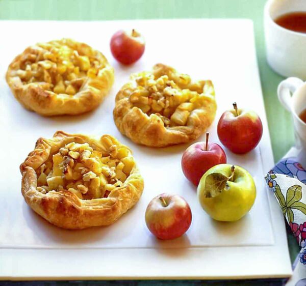 Three honey-ginger apple tarts on a white platter with 4 apples on the side.