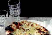 A wooden table with a white plate with parchment paper and Jim Lahey's white pizza, with a stack of glasses in the background.