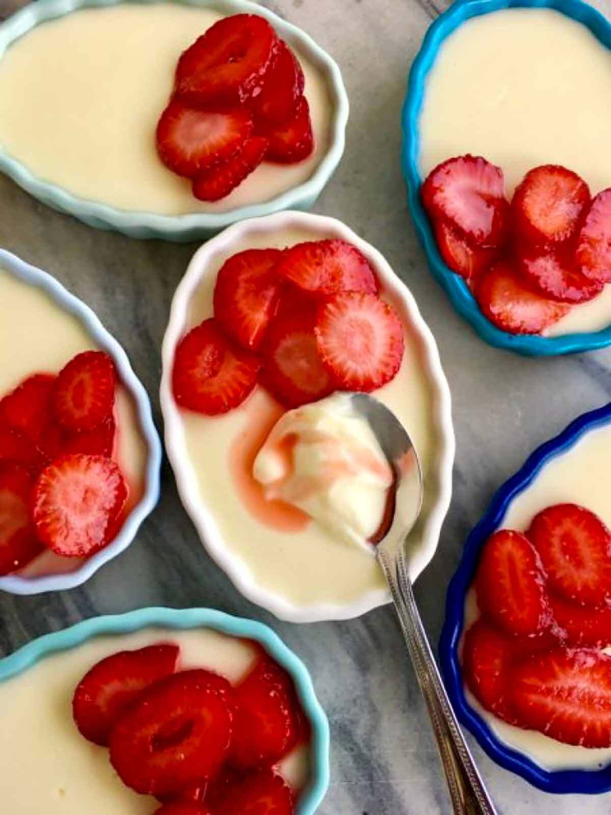 Six ramekins with lemon custard and strawberries on top.