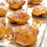A metal sheet pan covered with 8 golden and crisp chicken thighs.