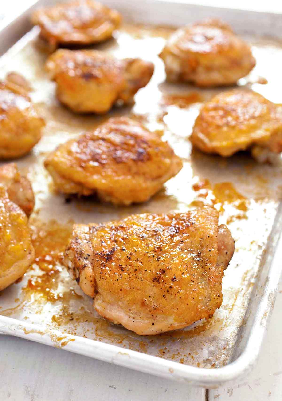 A metal sheet pan covered with 8 golden and crisp chicken thighs.