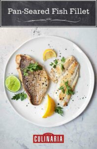 A white plate white 2 pieces of fish, one sliced and one whole with crisp skin attached. Garnished with slices of lemon, lime, and parsley.