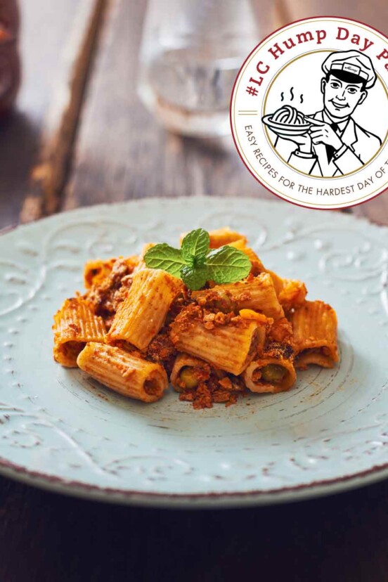 A light blue plate with a serving of rigatoni pasta covered with beef ragu, garnished with green herbs.