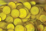 A close-up of a glass jar, filled with sliced, pickled zucchini and a few slices of onion.