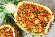 2 halves of a hollowed out pineapple filled with pineapple fried rice and garnished with green onions