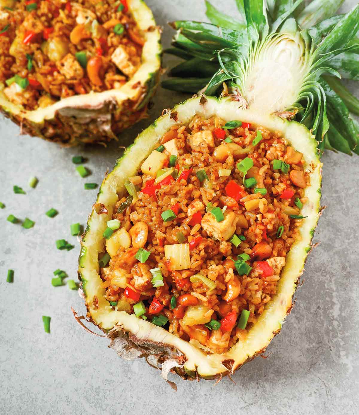 2 halves of a hollowed out pineapple filled with pineapple fried rice and garnished with green onions