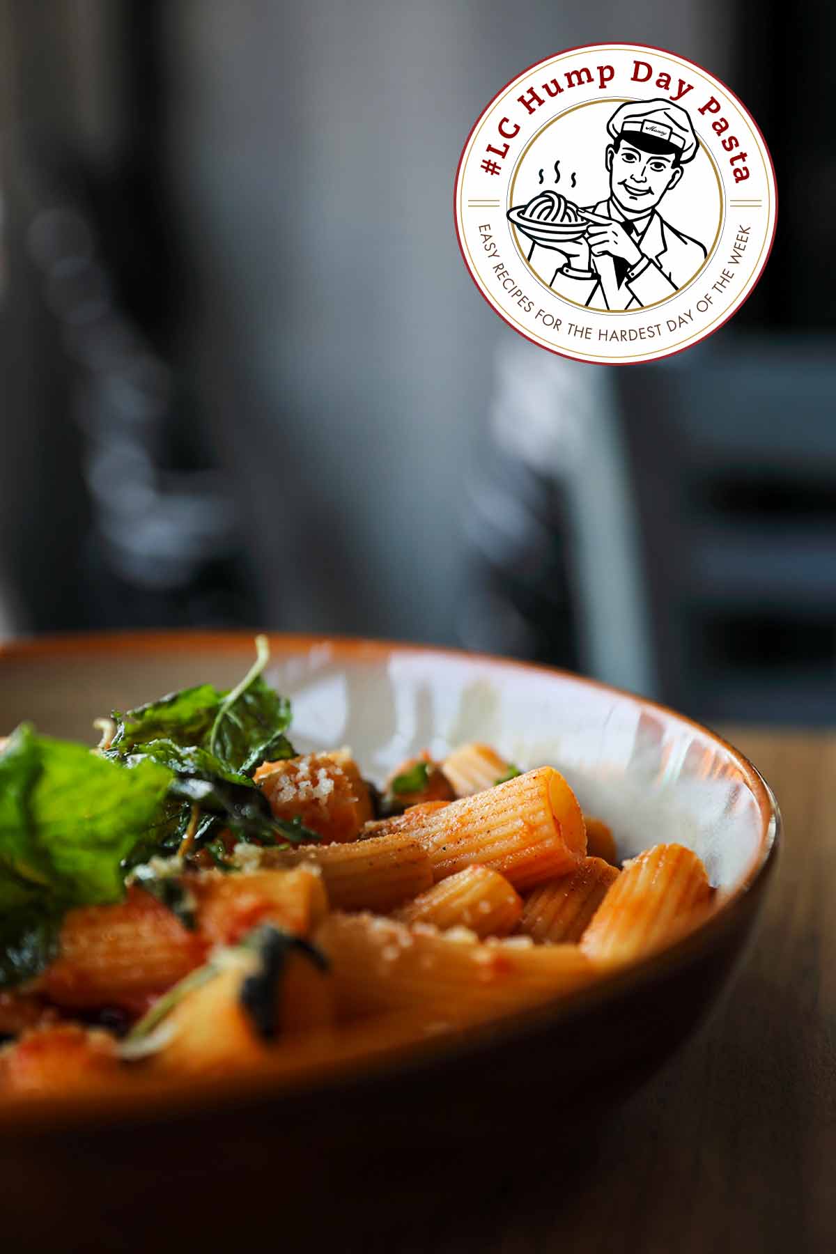 A close-up of a bowl filled with rigatoni noodles, covered with Parmesan cheese and basil.