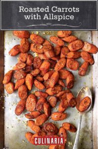 A large metal sheet pan filled with slices of roasted carrots with allspice, sea salt and preserved lemons, with a serving spoon.