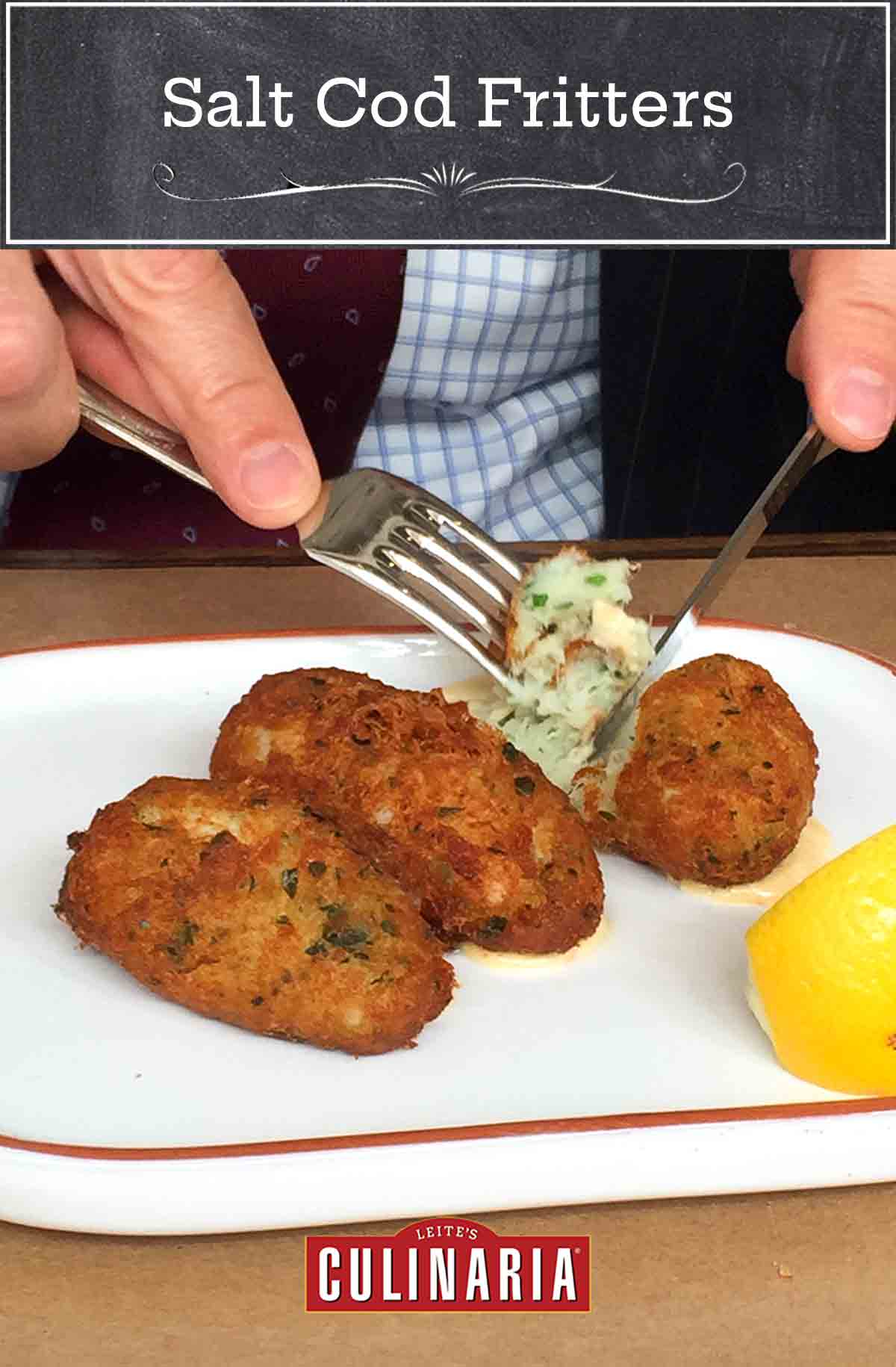 A close up of an oval plate with 3 pastéis de bacalhau, or Portuguese salt cod fritters, and a lemon wedge, one is being cut into with a knife and fork.