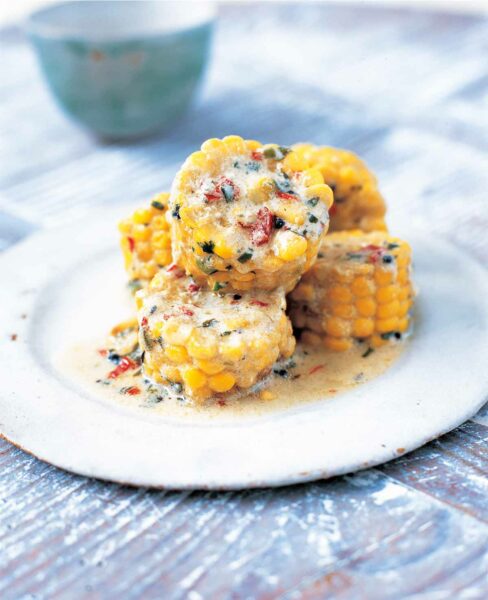 A white with 6 slices of corn on the cob, covered with coconut milk and a mixture of spices.