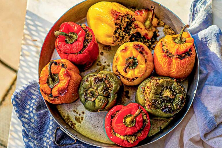 8 multicoloured stuffed peppers with turkey and quinoa in a metal dish, on a table with blue and white napkins.