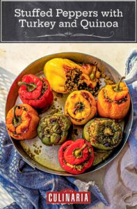 8 multicoloured stuffed peppers with turkey and quinoa in a metal dish, on a table with blue and white napkins.