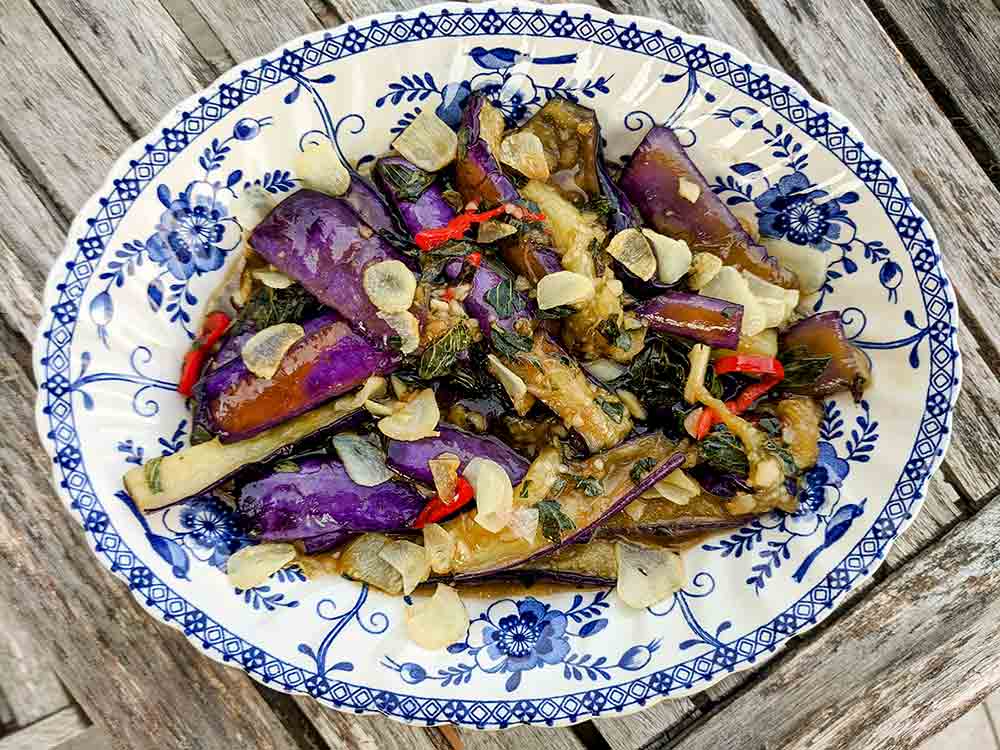 A large blue and white platter, filled with eggplant slices, garlic, chile, and basil.