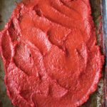 A metal sheet pan, covered with spread out tomato paste.