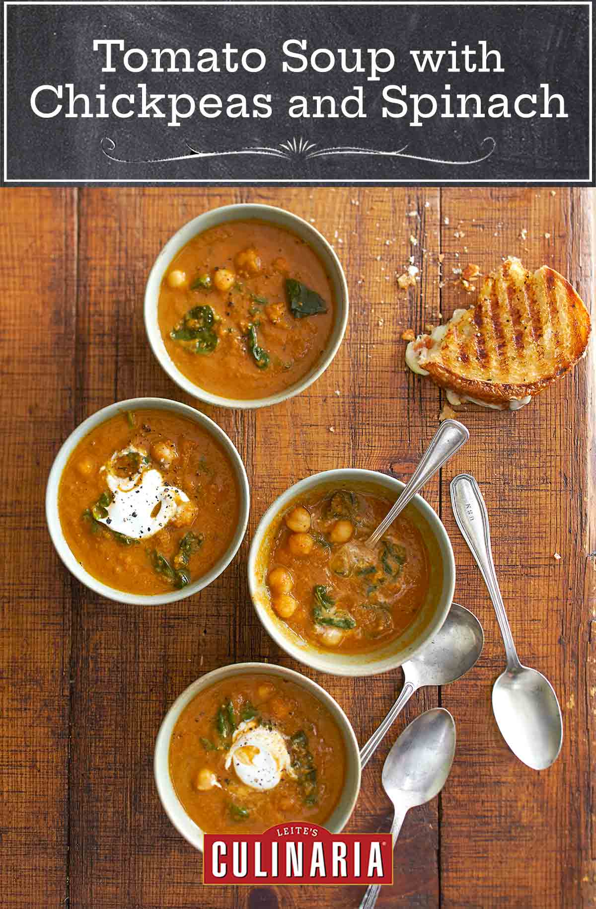 Three white bowls on a wooden table with soup spoons and half a grilled cheese sandwich. Each bowl is filled with tomato soup with chickpeas and spinach and topped with yogurt.