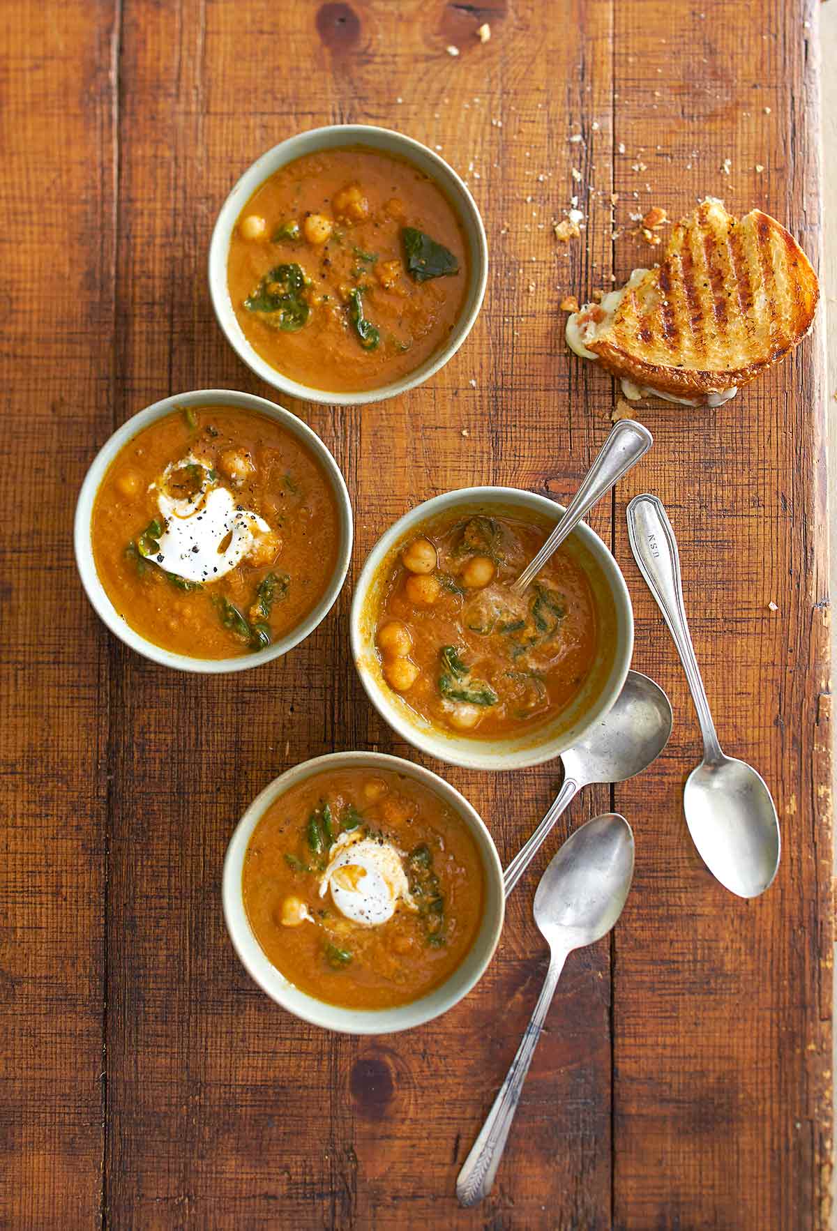 Each bowl is filled with tomato soup with chickpeas and spinach and topped with yogurt.