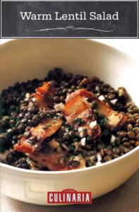 A creamy pottery bowl filled with a warm lentil salad, made with green and brown lentils, bacon, shallots and chives.