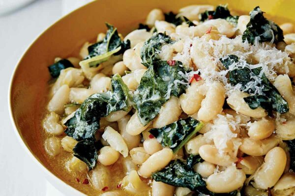 A bowl of white beans and Tuscan kale, sprinkled with grated Parmesan cheese.