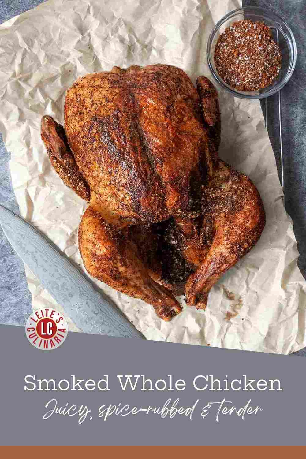 A whole smoked chicken with a crispy spice-rubbed skin sits on crumpled parchment paper next to a bowl of dry rub.