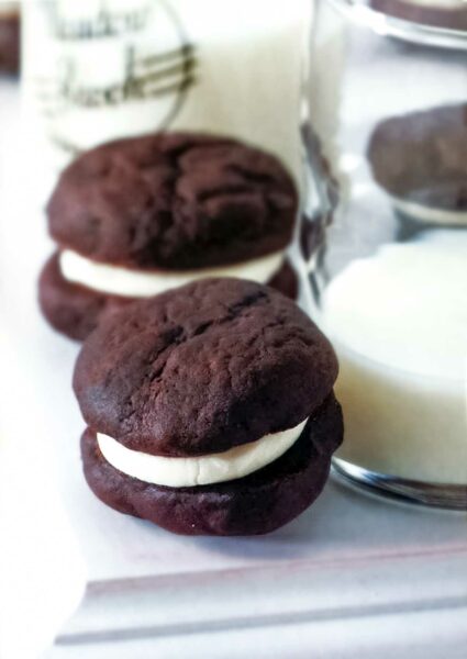 2 dark chocolate sandwich cookies filled with white cream filling, leaning against a glass of milk.
