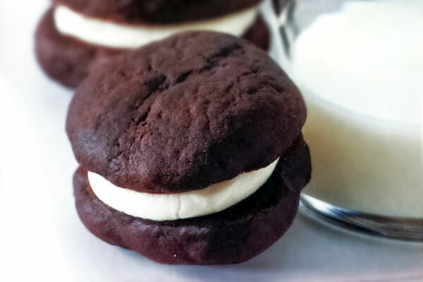 2 dark chocolate sandwich cookies filled with white cream filling, leaning against a glass of milk.