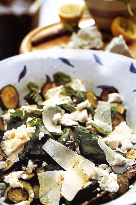 A blue and white bowl with zucchini coins, cheese, basil, and mint.