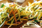 Close up of a pile of zucchini slaw with carrots, squash, and bell peppers, sprinkled with parsley. 2 forks in the background.