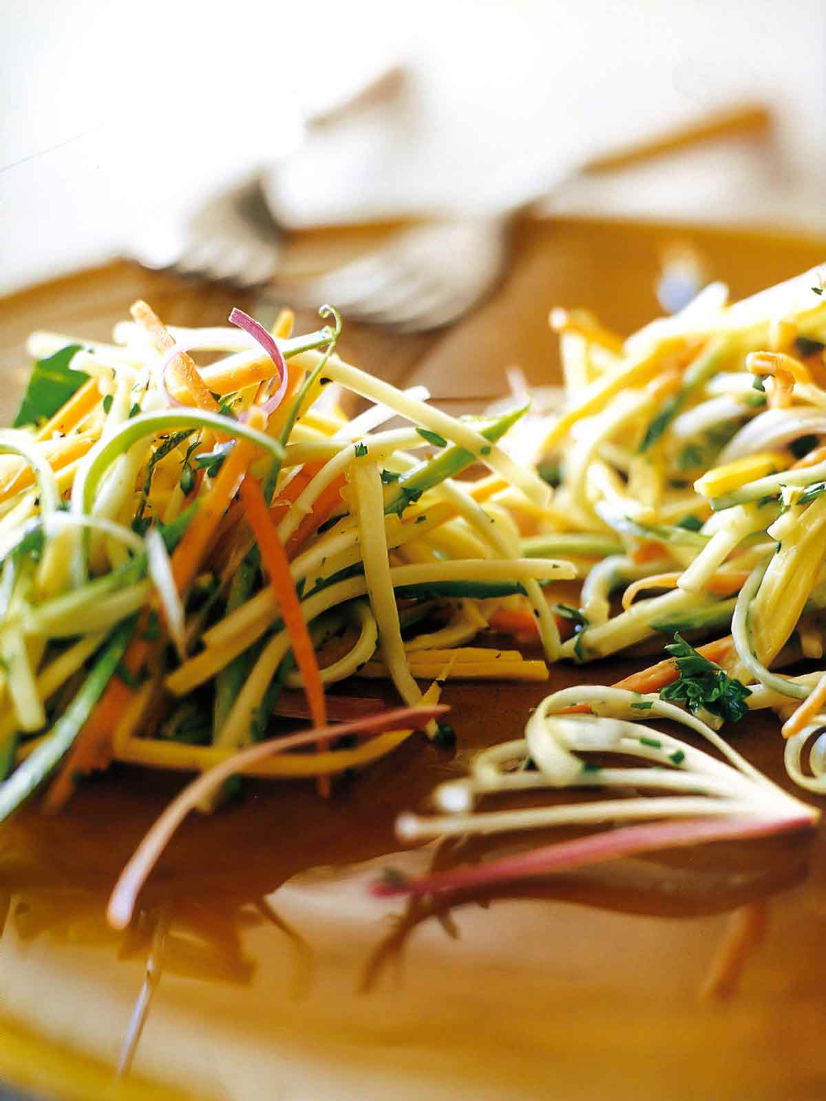 Close up of a pile of zucchini slaw with carrots, squash, and bell peppers, sprinkled with parsley. 2 forks in the background.