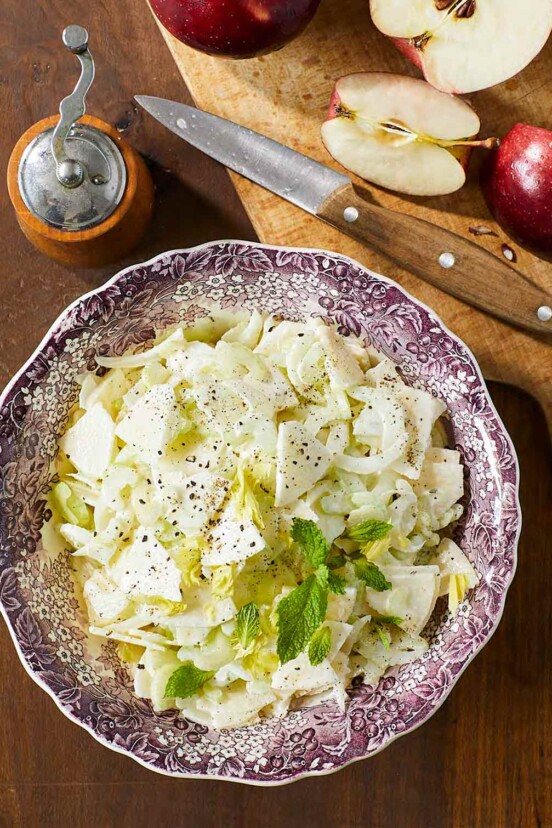 Apple and celery salad in a patterned bowl, beside a cutting board with a knife and apple slices.