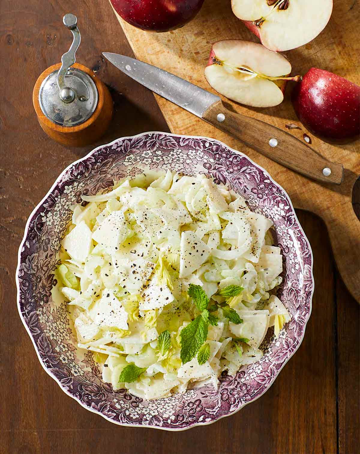 Apple and celery salad in a patterned bowl, beside a cutting board with a knife and apple slices.