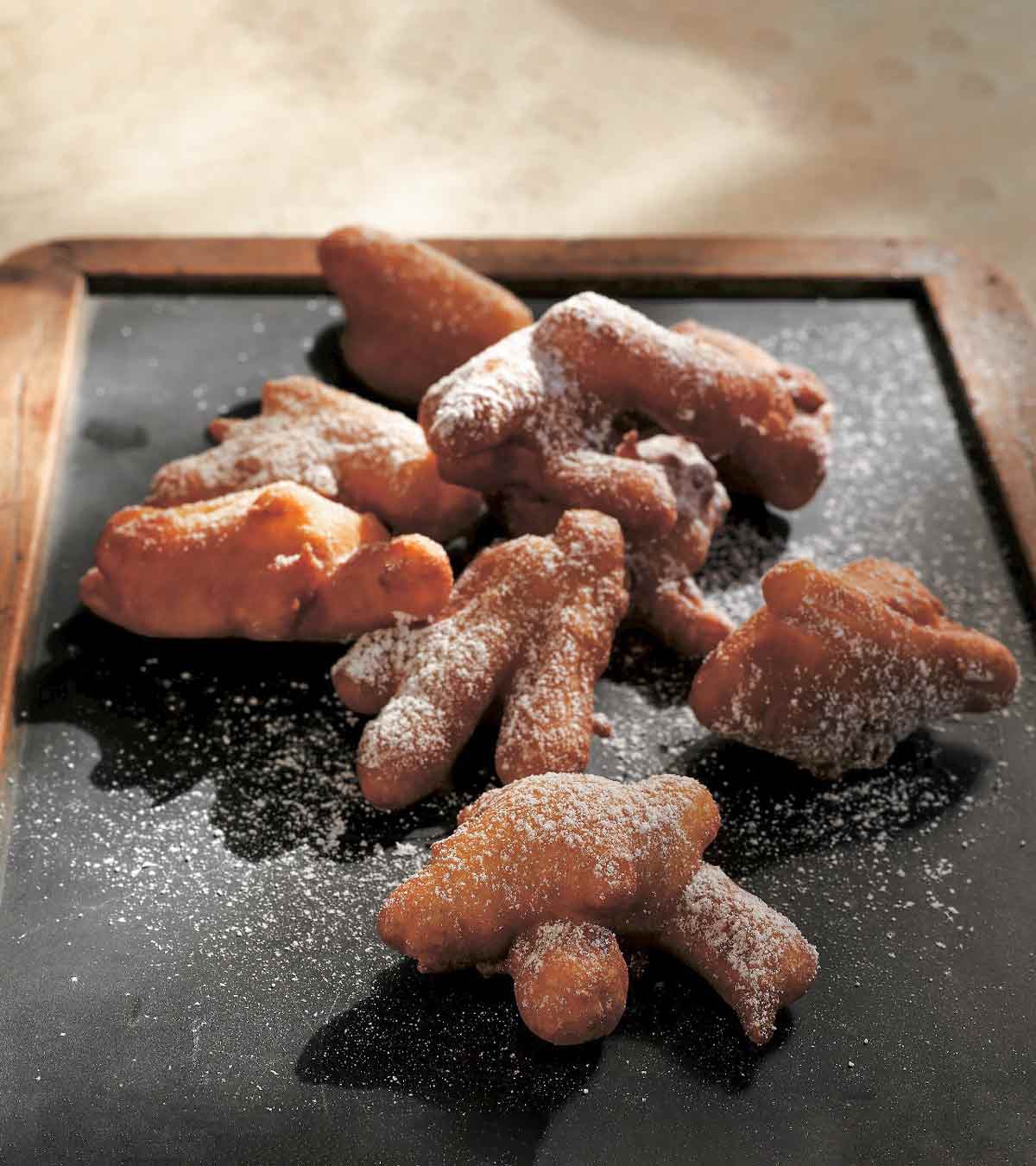 A slate tray with piles of matchstick sliced apple fritters, dusted with icing sugar.