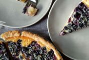 A blueberry custard pie in a pie plate, with 2 dessert plates with a slice of pie on them, one with a fork and a bite missing.
